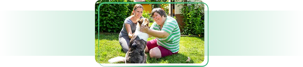 Two women with a dog in the grass.