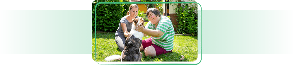 Two women with a dog in the grass.