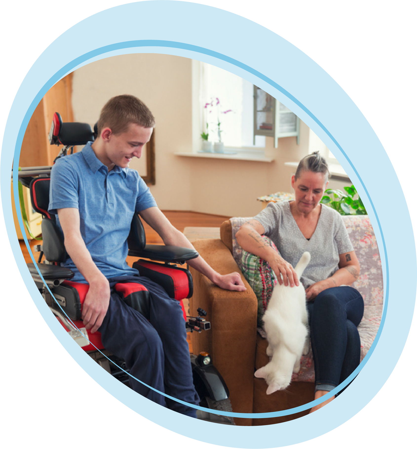 Young man in wheelchair with caregiver and cat.