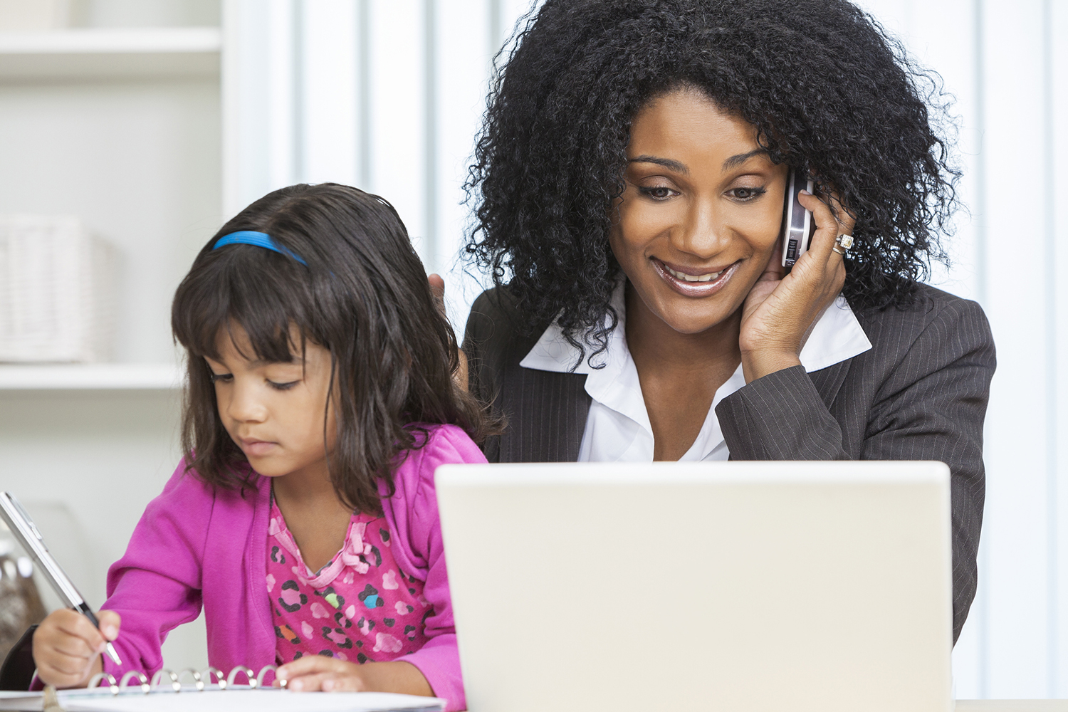 Mother sitting with daughter while talking on the phone and looking at a laptop