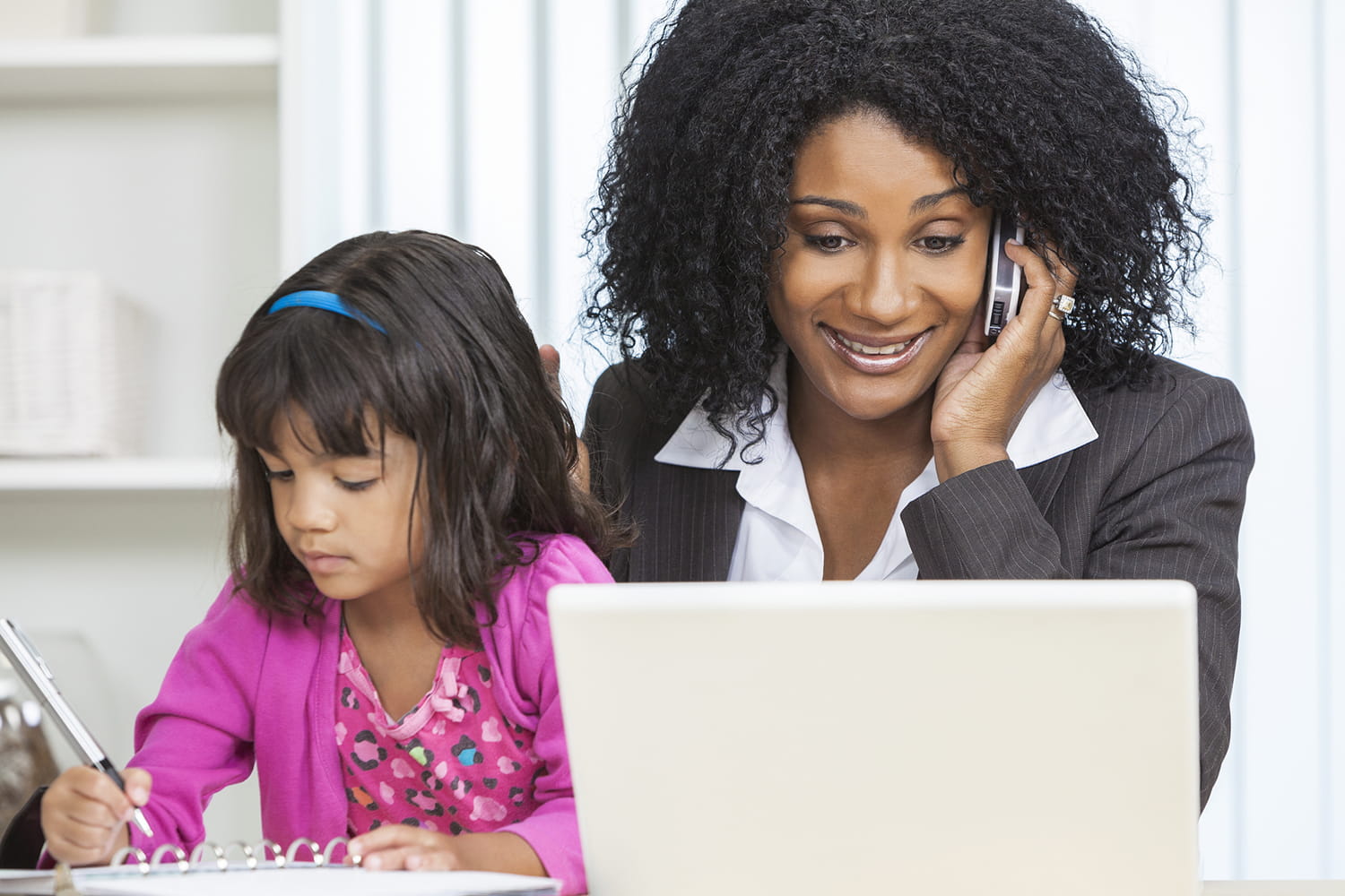 Mother sitting with daughter while talking on the phone and looking at a laptop