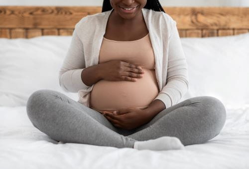 pregnant woman sitting cross legged with hands holding belly