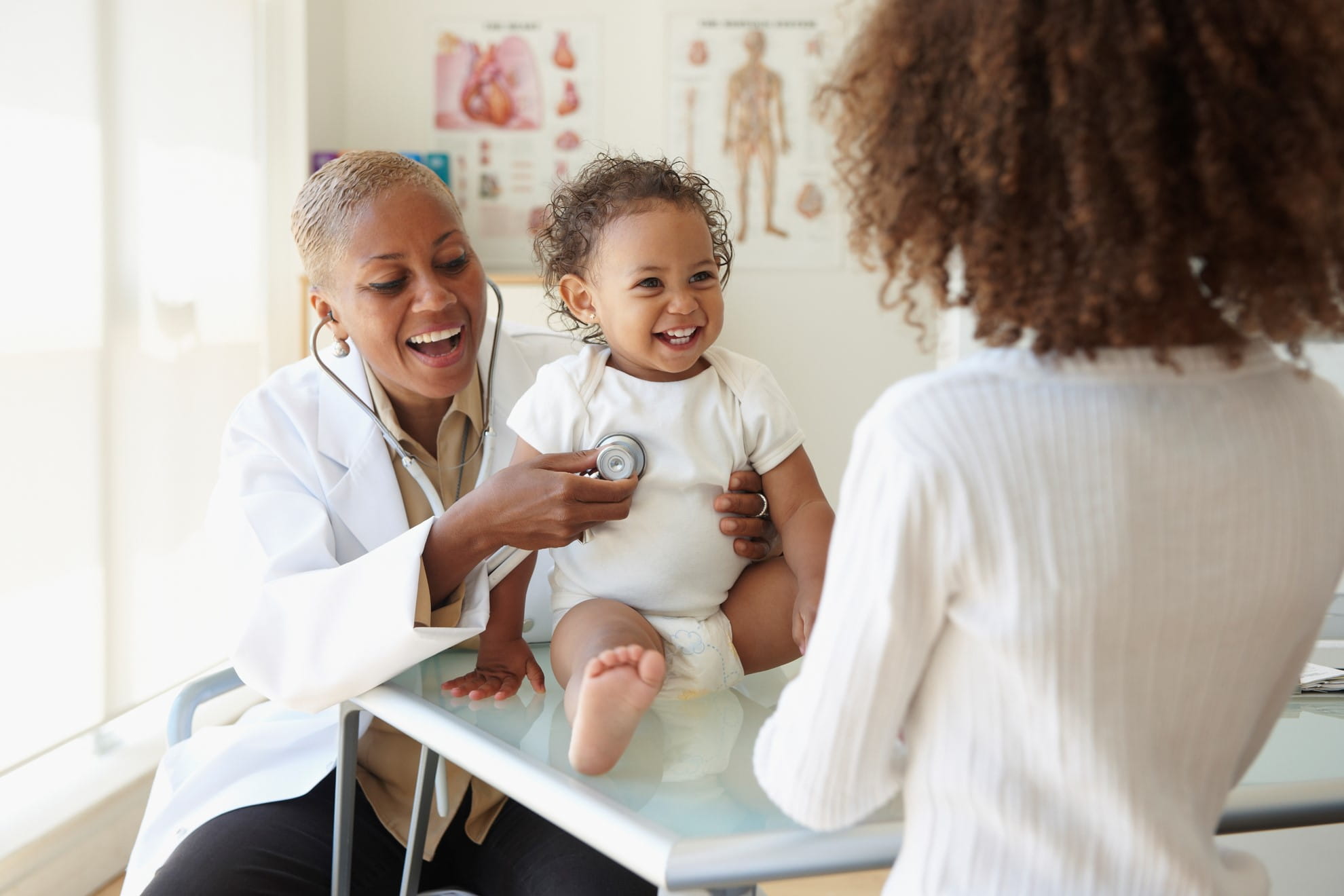 Doctor and mom watching sitting baby in clinic. 