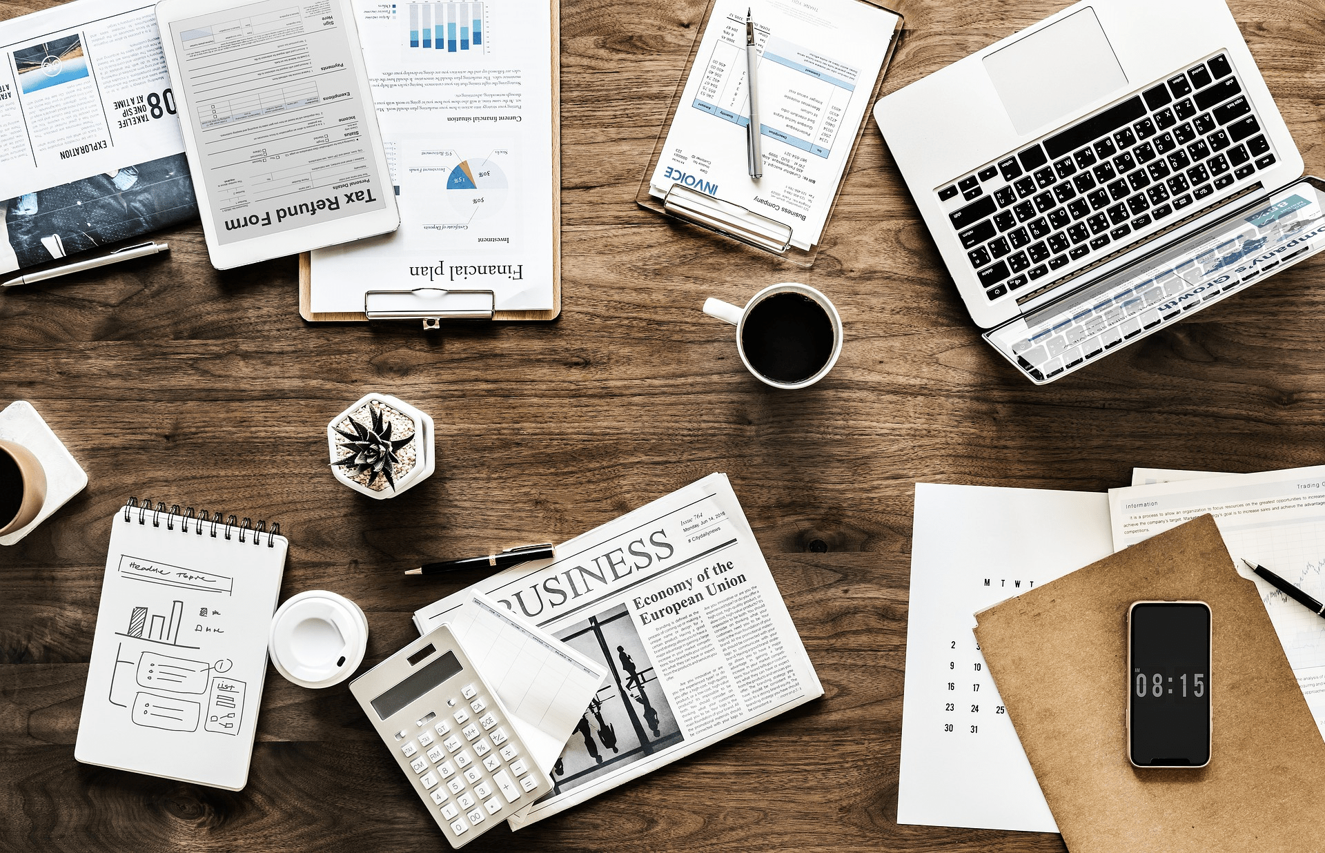 business paperwork, laptop, coffee cup, and other items on desktop