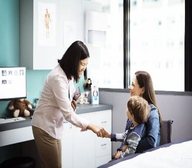 Doctor greeting boy sitting on mother in clinic