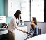 Doctor greeting boy sitting on mother in clinic