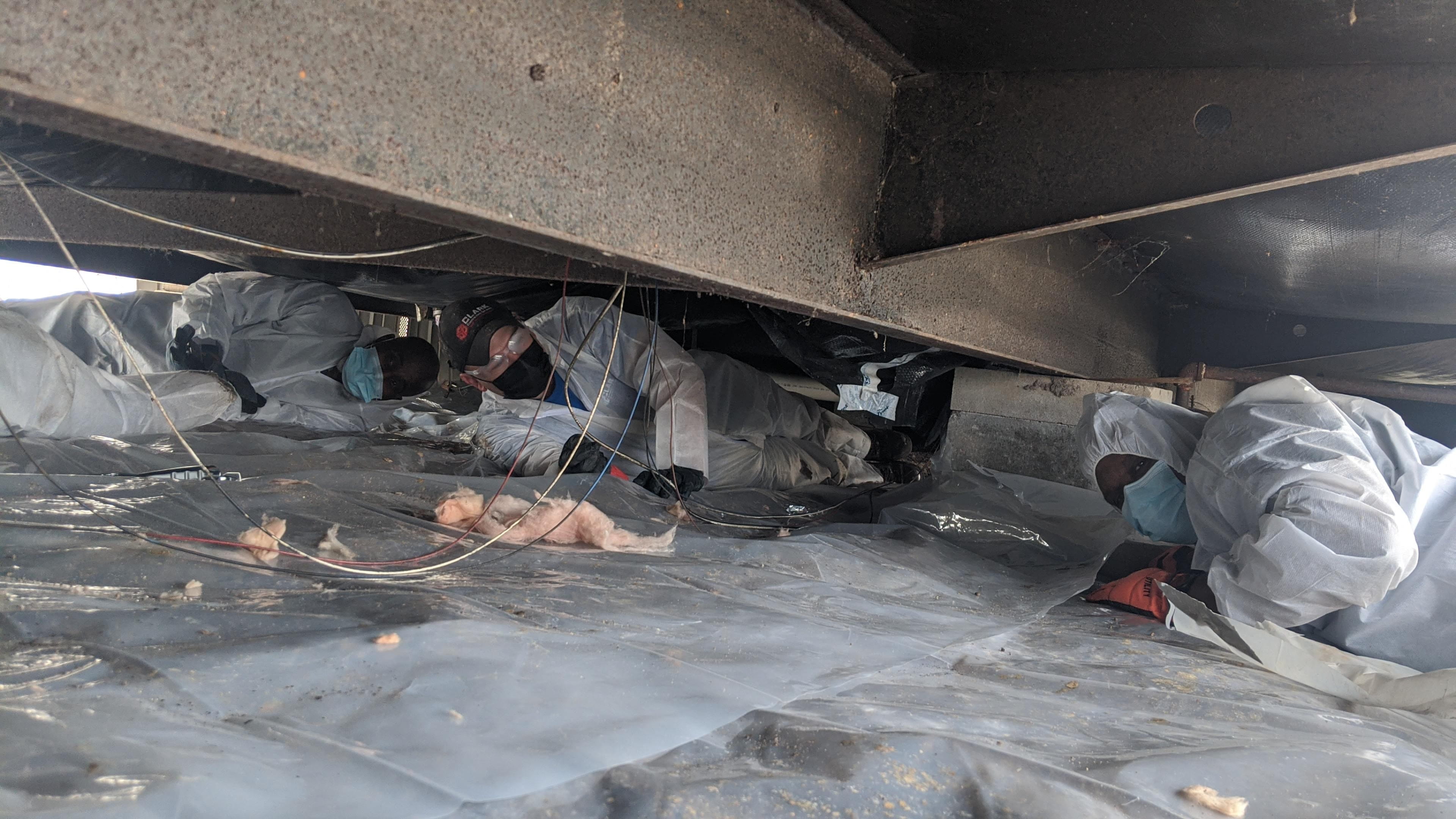 Weatherization workers installing vapor barrier under a mobile home