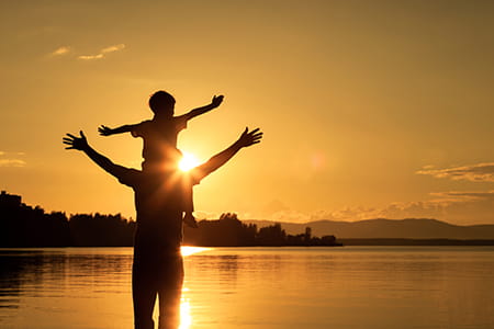 man with child on shoulders arms upheld at sunrise