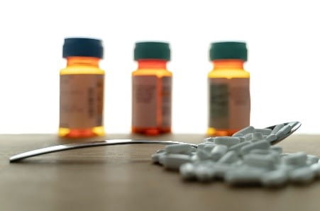 Pills heaped over a spoon with medication vials in the background