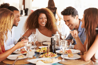Group of five young friends laughing and enjoying a meal in a casual restaurant