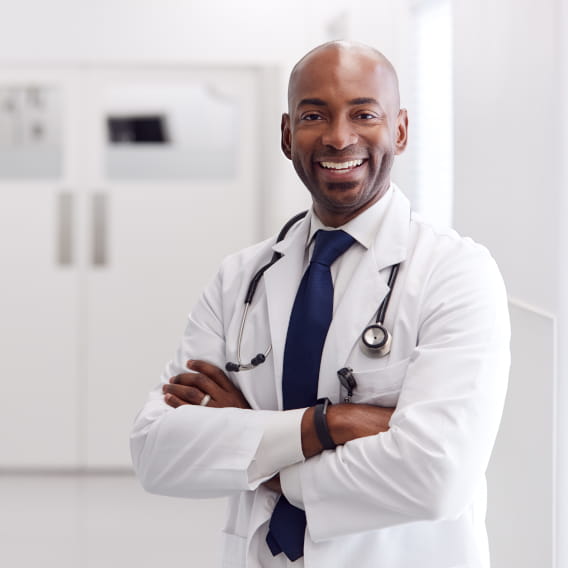 Black/African American male healthcare provider in white coat with arms crossed, smiling at camera