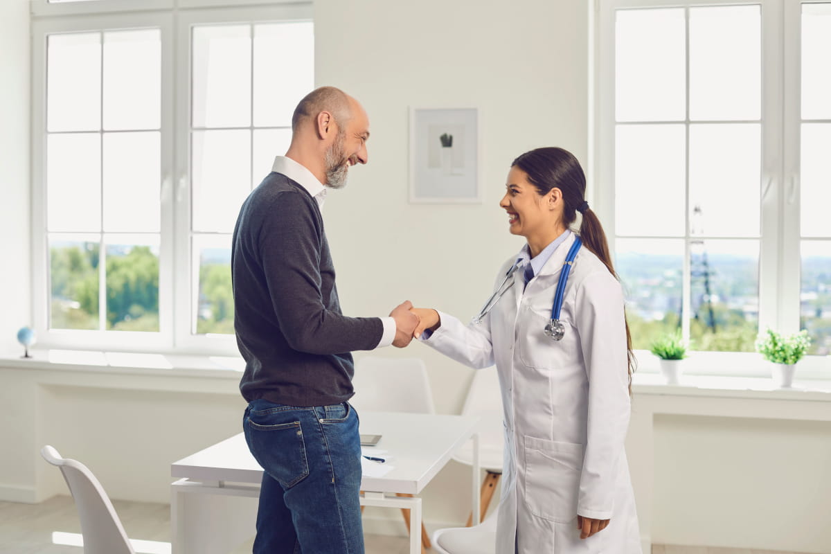 Female healthcare provider and male patient shaking hands while standing in an exam room