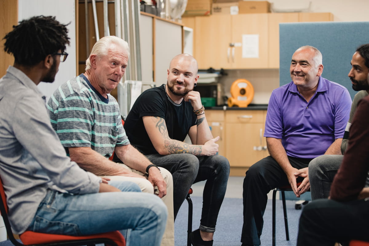Group of men seated in a circle listening in support.