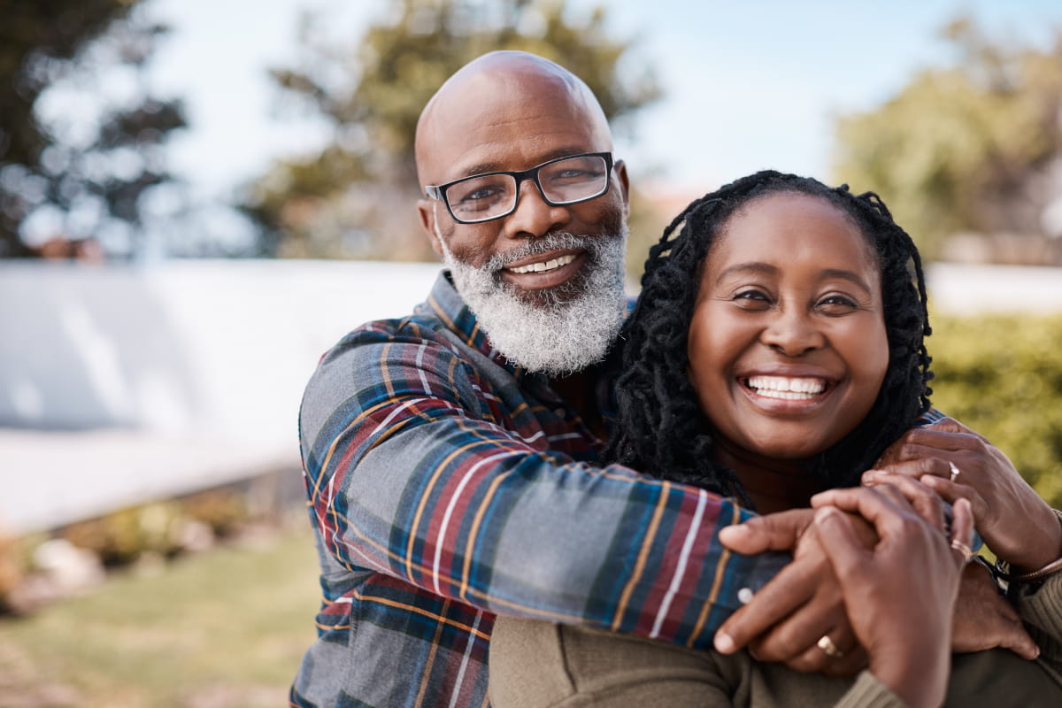 Black American middle-aged man smiling and hugging a Black American middle aged woman from behind