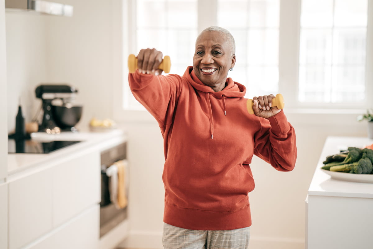 Senior woman standing in kitchen and exercising with hand weights 