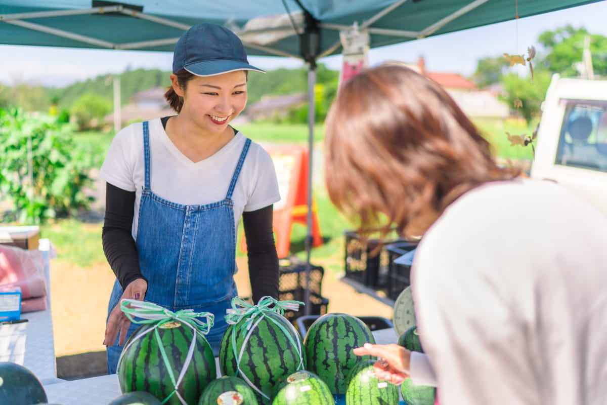 Two women at a farm market gathered around watermelons