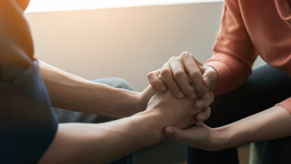 Close-up of a seated person holding the hand of another seated person for encouragement