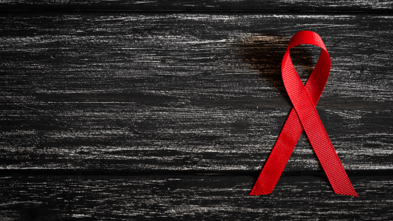 A red AIDS ribbon with a black wood backdrop