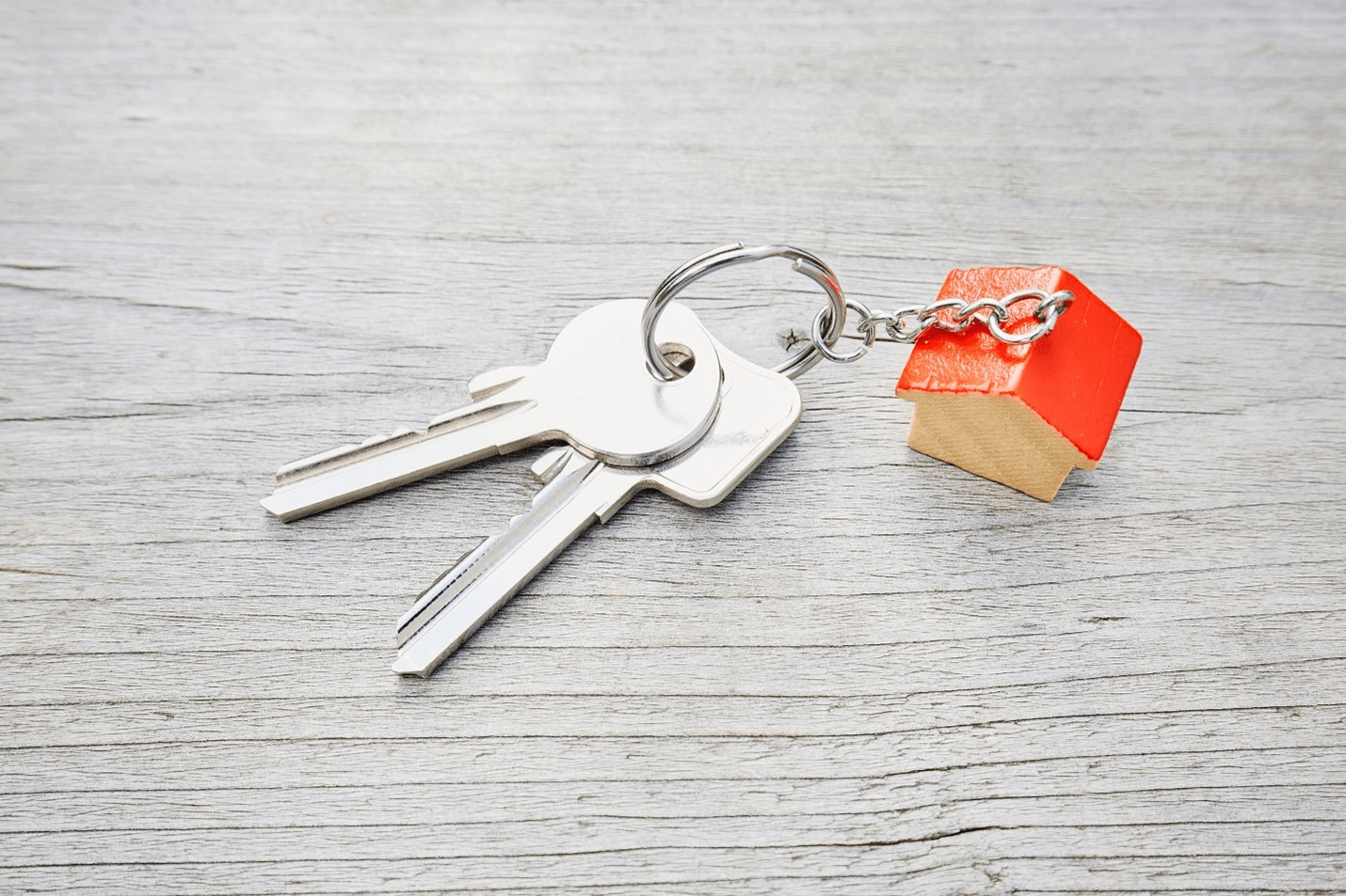 two keys on a keychain with a wooden toy house with orange roof attached to chain