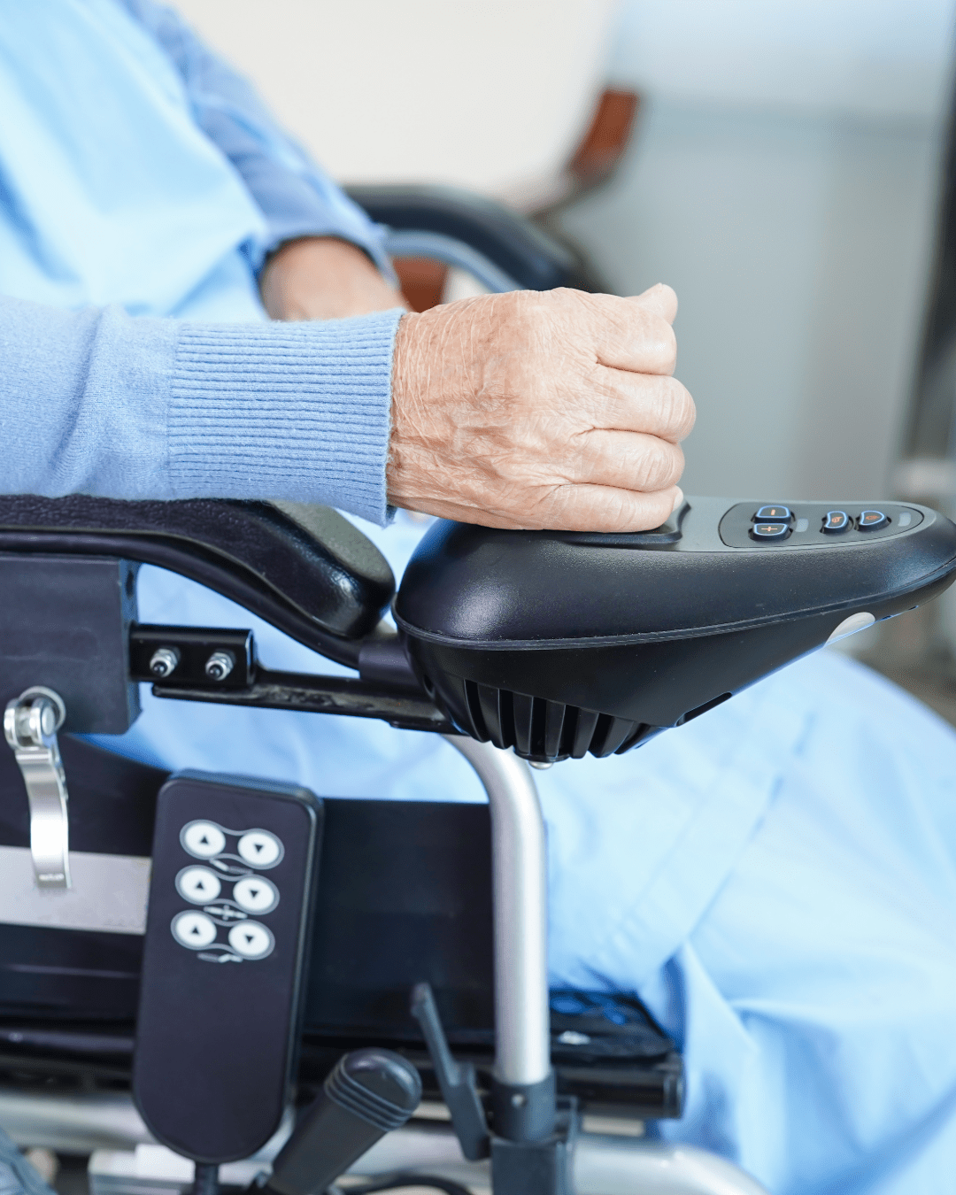 Close-up of a person’s hand resting on the joystick control of a power wheelchair.