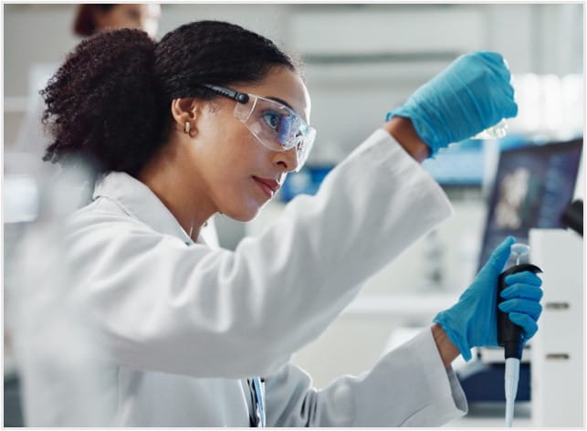 Scientist looking at a vial of liquid while holding a pipette in her other hand