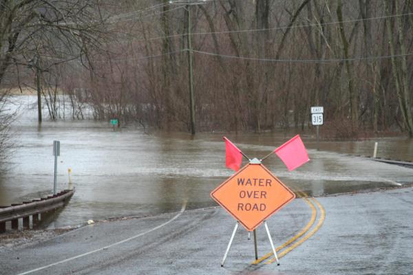 Road submerged in floodwater, with a sign reading 