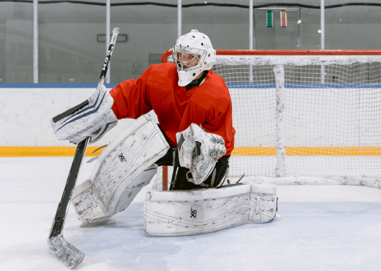 Image of hockey goalie in a red jersey and full gear blocking a puck in the net
