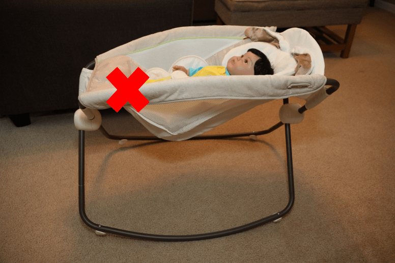 Baby doll placed in an inclined sleeper. There is an x over the inclined sleeper because it is not a safe sleep environment. 