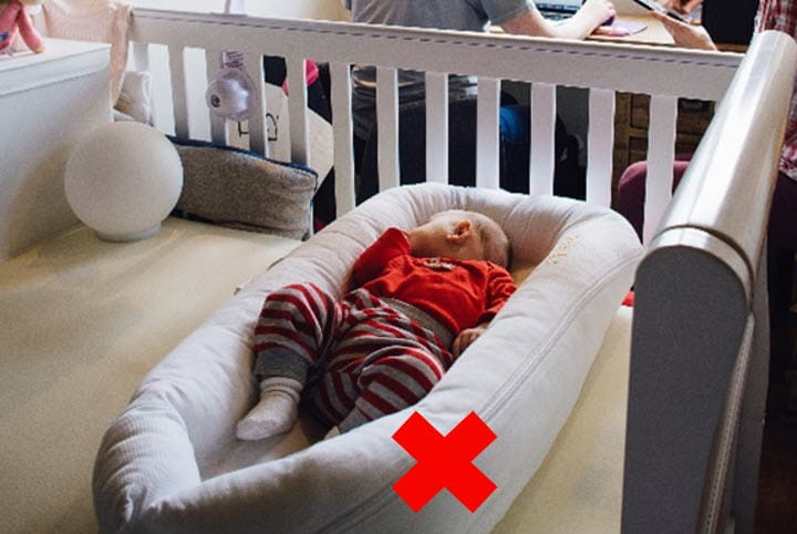 Infant sleeping in a pillow-like bed called a dock. There is an x over the dock because it is not a safe sleep environment.