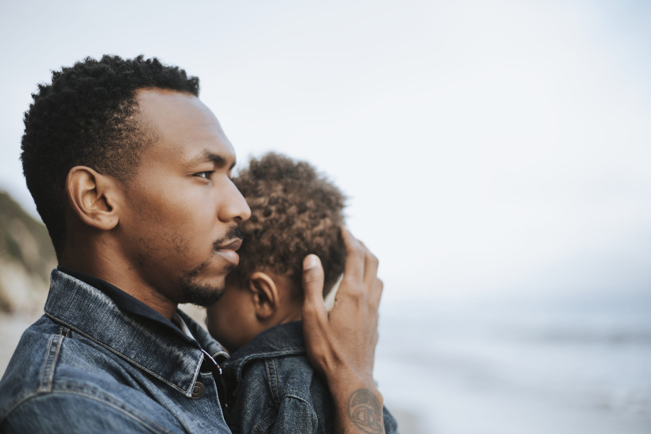 young man holding infant to him at lakeshore