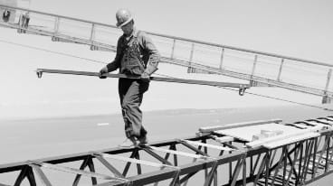 Workman crossing cross bridge between catwalks near top of North tower.