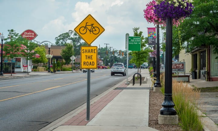 A yellow Share the Road bicycle sign on a quiet road.