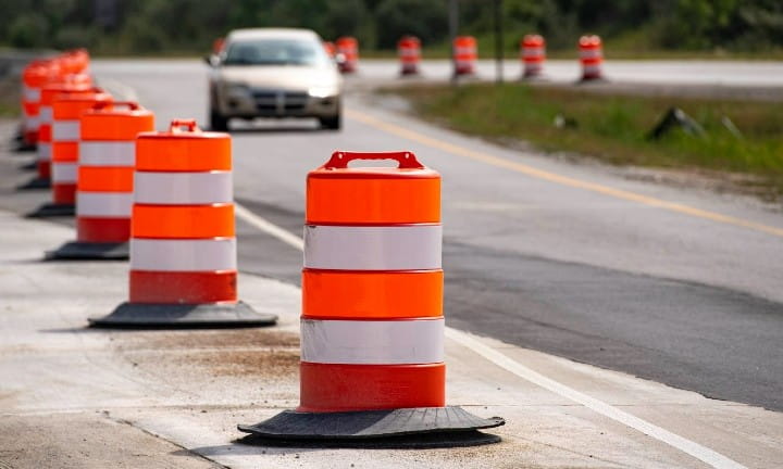 A vehicle driving through a work zone set up with barrels. 