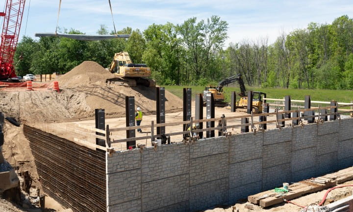 A crane and workers placing segments of a soundwall.
