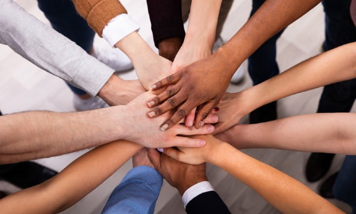A diverse group of multicultural people putting their hands together in a huddle. 