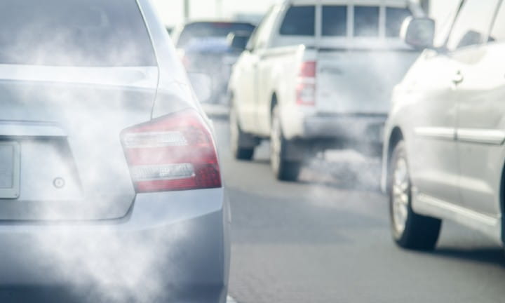 Several vehicles sitting in traffic with exhaust coming from their tailpipes.