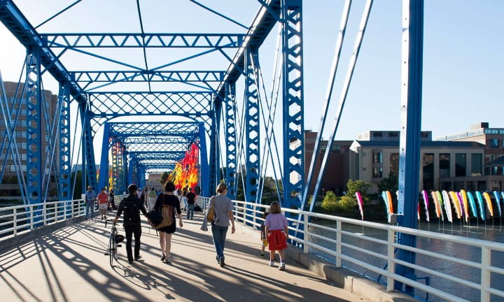 Pedestrians walking across a blue bridge in Grand Rapids.