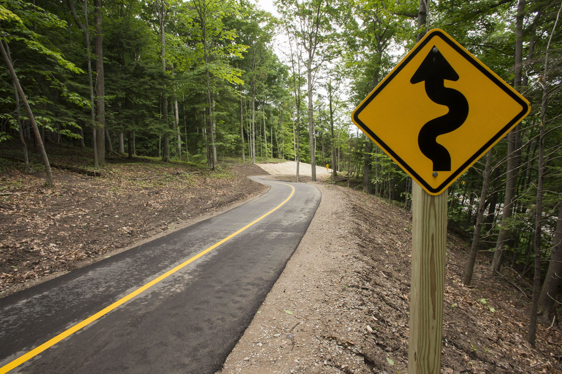 Sign along the side of a bicycle lane through the woods. 