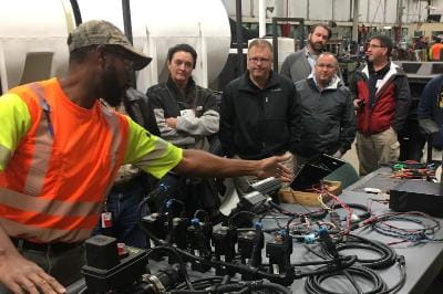 A group of people listening to an employee who is demonstrating some equipment.