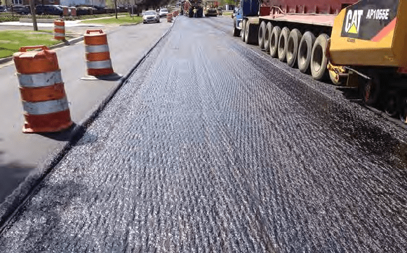 Pavement maintenance project in process with traffic drums and machinery at the site.