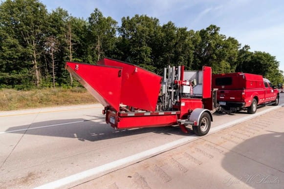 A FWD test machine on a trailer towed by a truck on a concrete-paved roadway.
