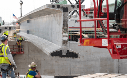 Construction workers stand by as a concrete I-beam is placed.