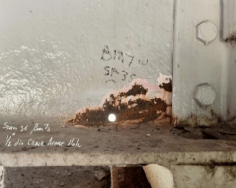 A close-up of a crack on a steel bridge beam end.
