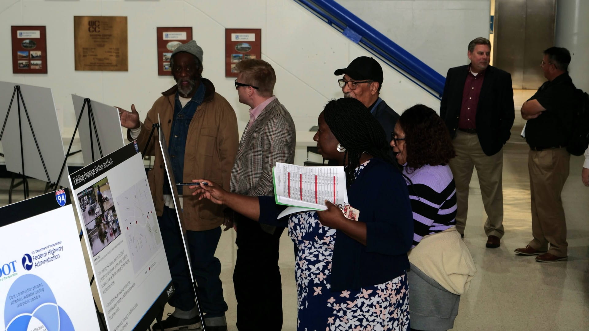 A diverse group of community members gather around I-94 public meeting boards.