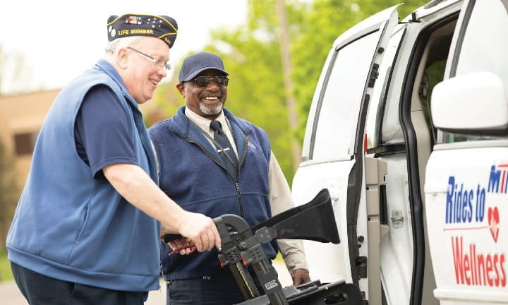 A Rides to Wellness driver assists a passenger with his walking assistance device.