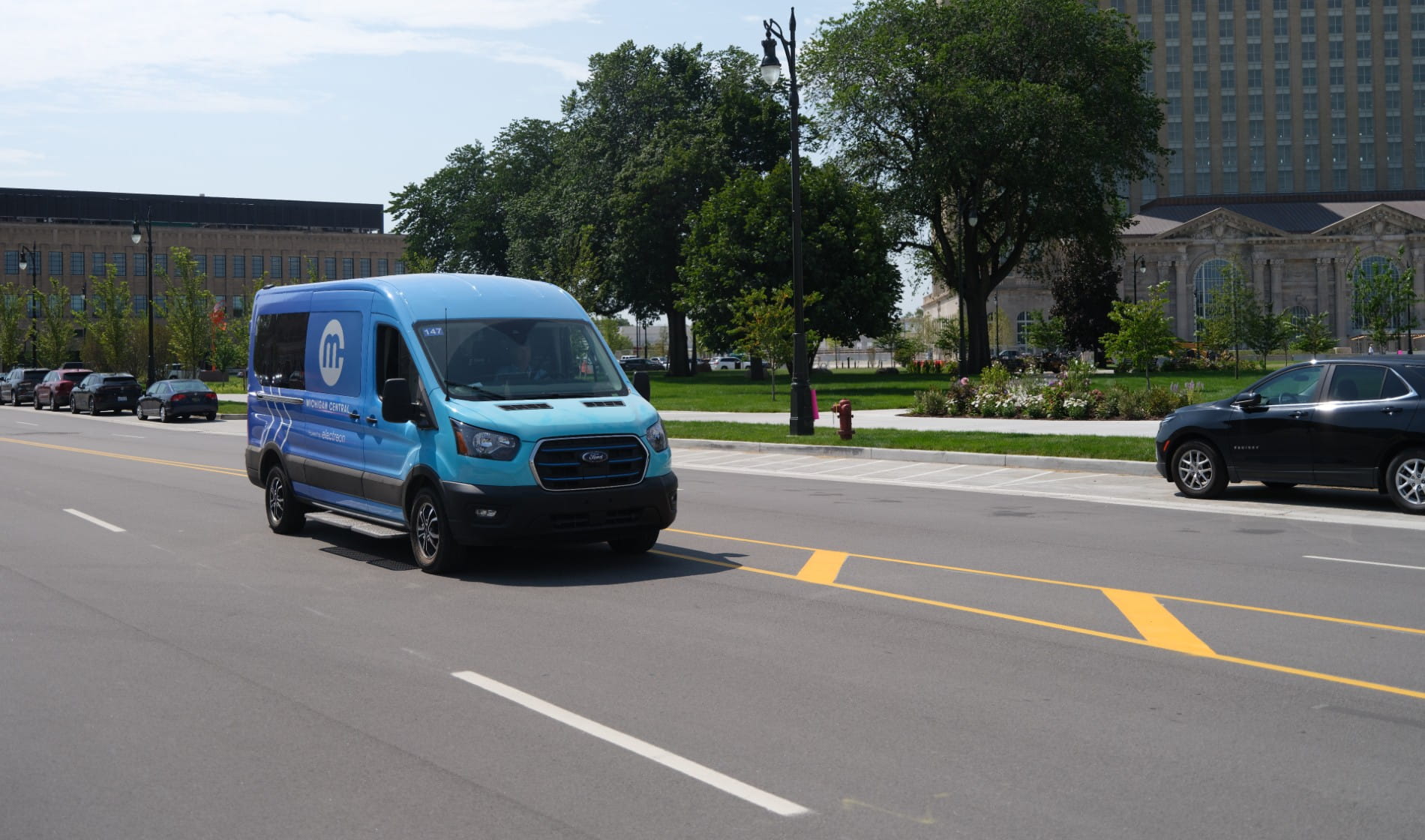 Ford EV Transit dynamically charges over wireless charging road on 14th street; Michigan Central pictured in background.