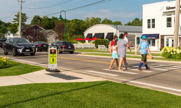 A family crossing a busy road at a designated pedestrian crosswalk area.