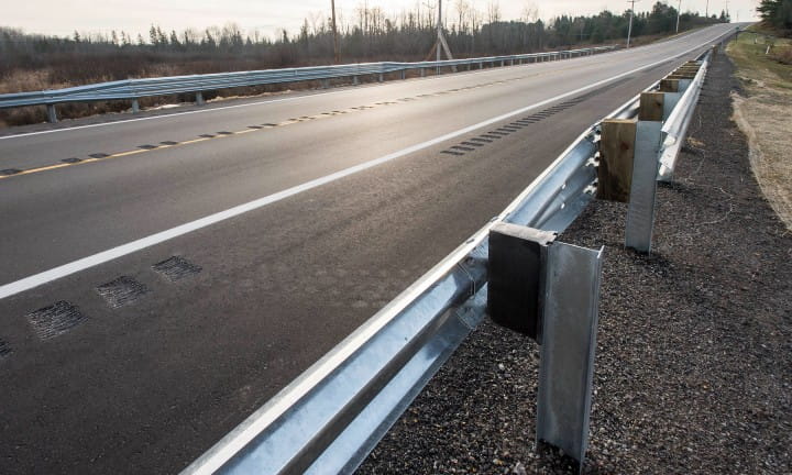 A newly paved road with rumble strips and guardrail for safety.