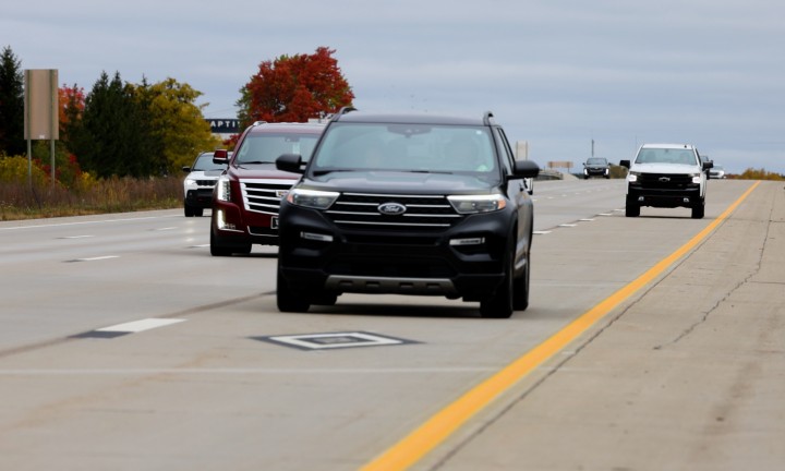 A black vehicle with two occupants driving in an HOV lane indicated with a diamond road marking.