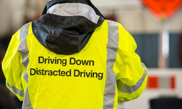 A road worker wearing a high visibility coat that reads Driving Down Distracted Driving at a Work Zone Awareness Week event.